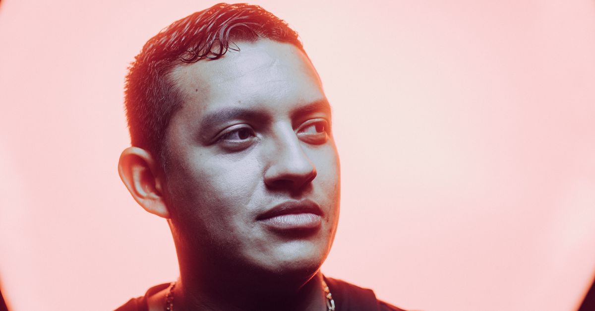 Close-up portrait of a young man with a stylish necklace against a pink background, emphasizing modern fashion.